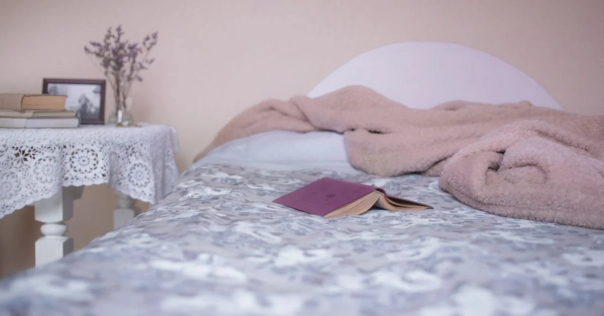 Un intérieur de chambre cosy avec un lit confortable, un livre ouvert et une table recouverte de dentelle pour la détente.