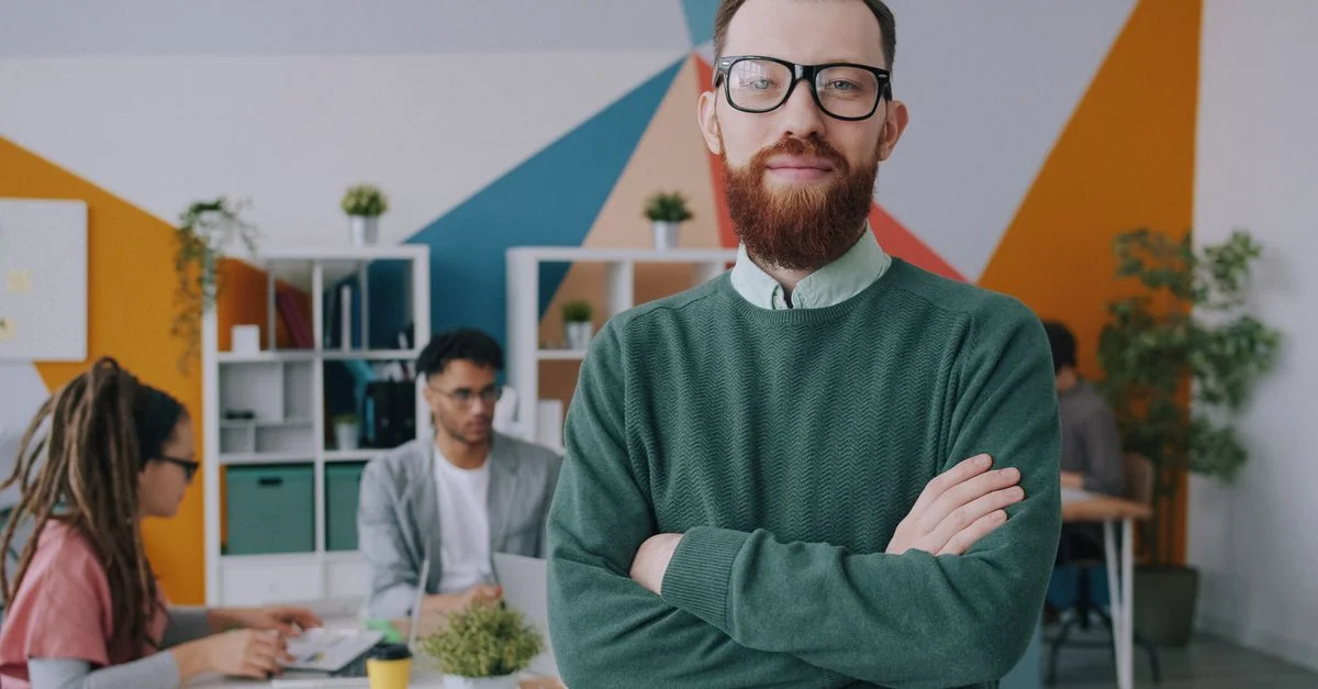 Portrait d'un professionnel sûr de lui dans un environnement de bureau créatif, avec ses collègues travaillant en arrière-plan.