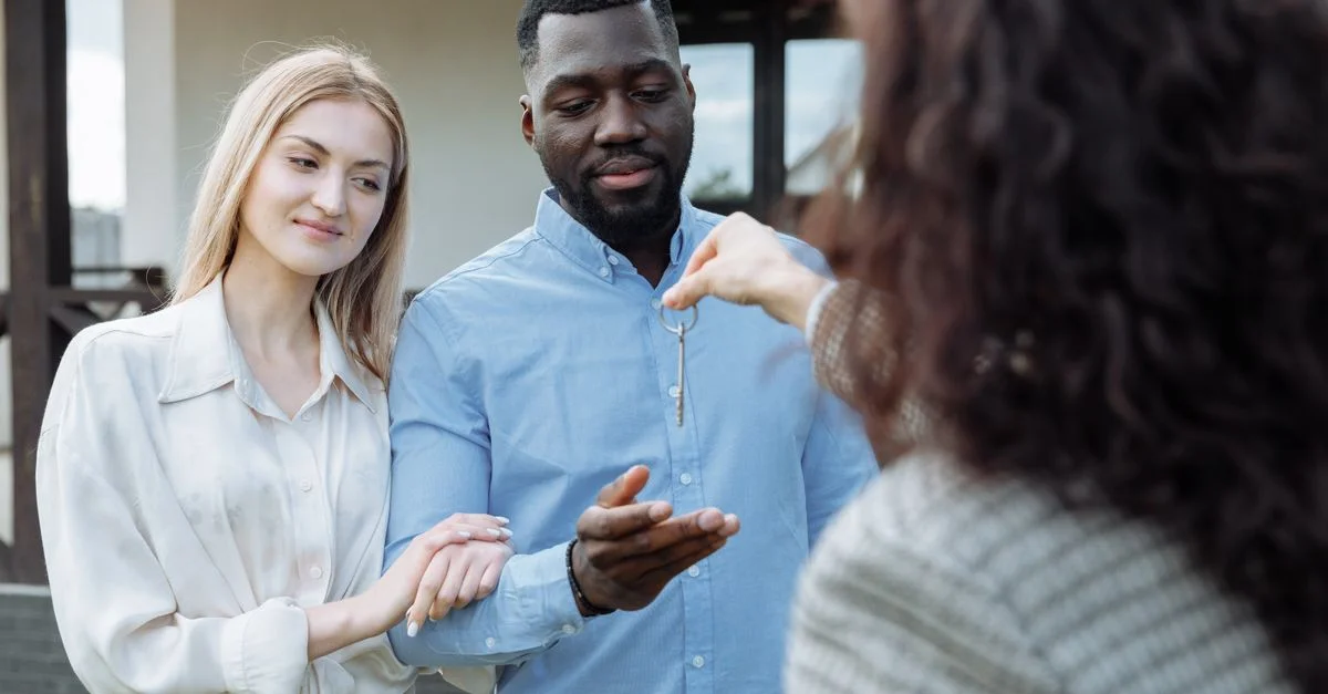 Un couple heureux recevant les clés de leur nouvelle maison de la part de l'agent immobilier en plein air.