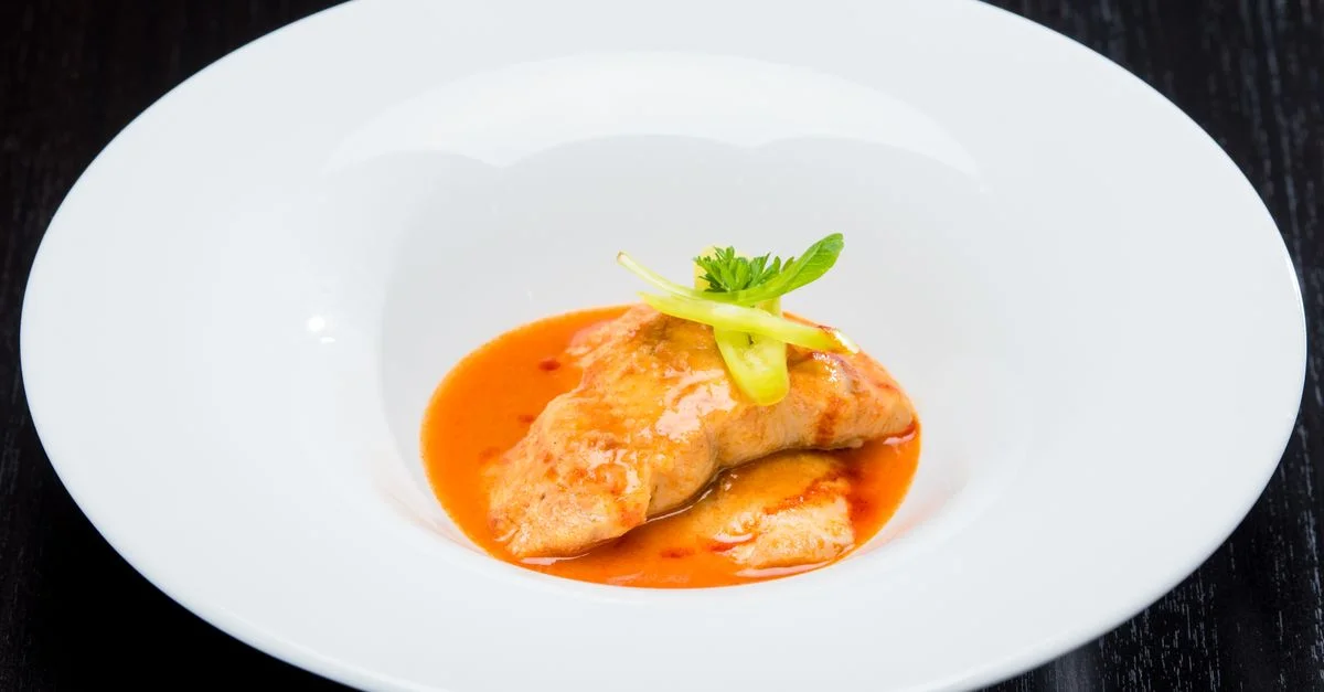 Un filet de poisson gourmet avec une sauce tomate riche, garni d'herbes, servi dans un plat blanc.