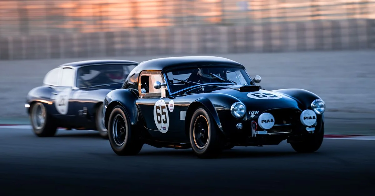 Deux voitures classiques s'affrontent intensément sur une piste au coucher du soleil, mettant en valeur la vitesse et la compétition.