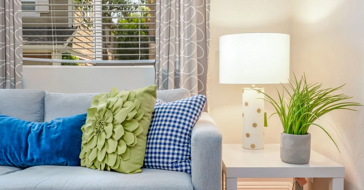 Salon lumineux avec un sofa doux, des coussins colorés, une lampe de table élégante et une plante verte luxuriante.