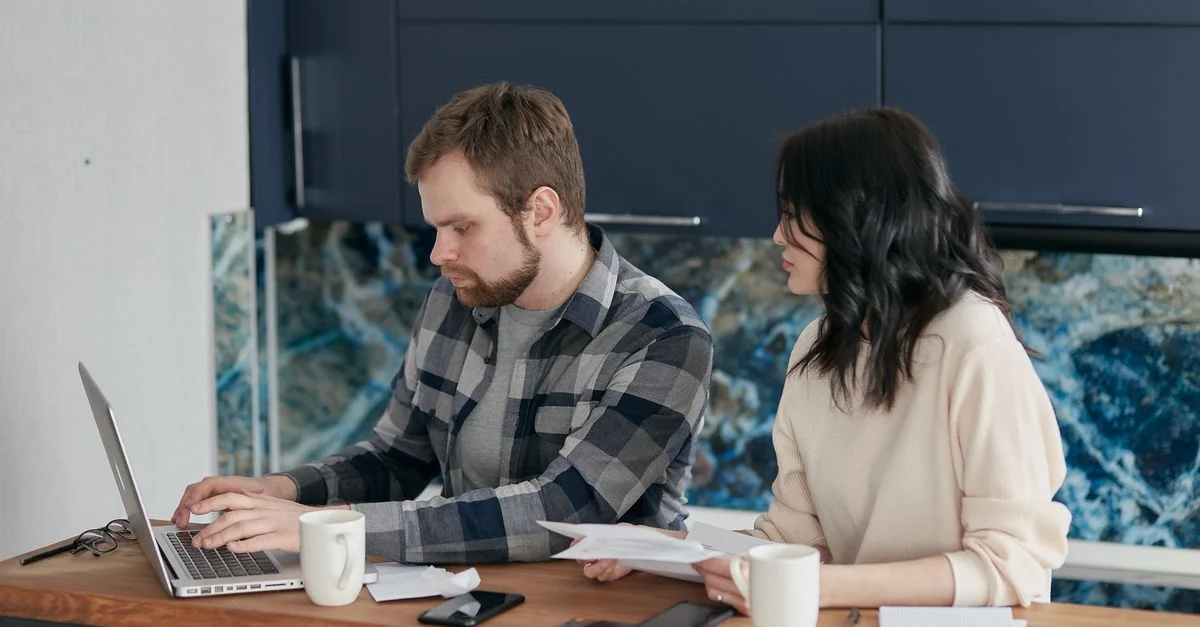 Un couple passe en revue les factures et les finances à un bureau avec un ordinateur portable et des papiers. Cadre intérieur, axé sur la budgétisation.