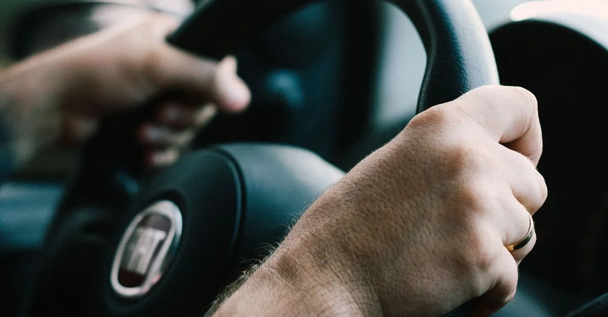 Mains fermement agrippées à un volant de voiture, prêtes à conduire.